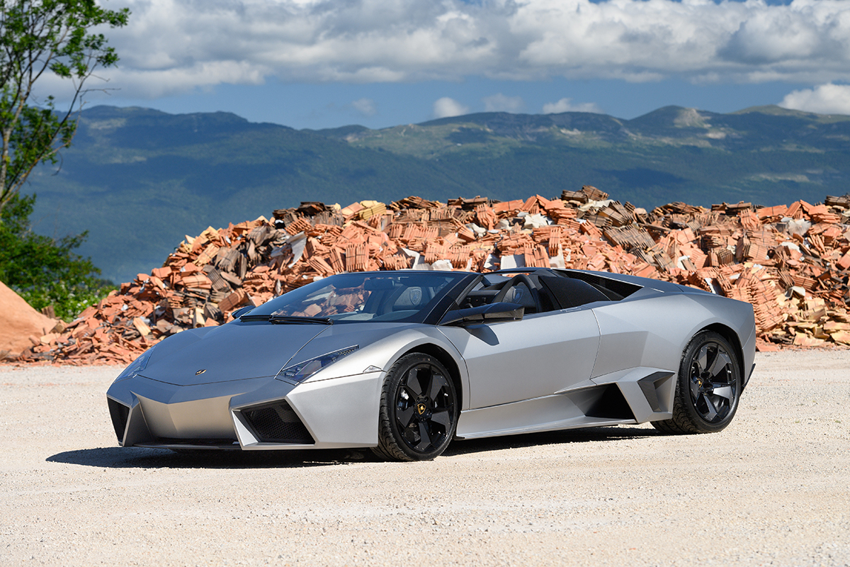 silver 2010 Lamborghini Reventon Roadster 6 with a pile of orange stones behind it and mountains in the background