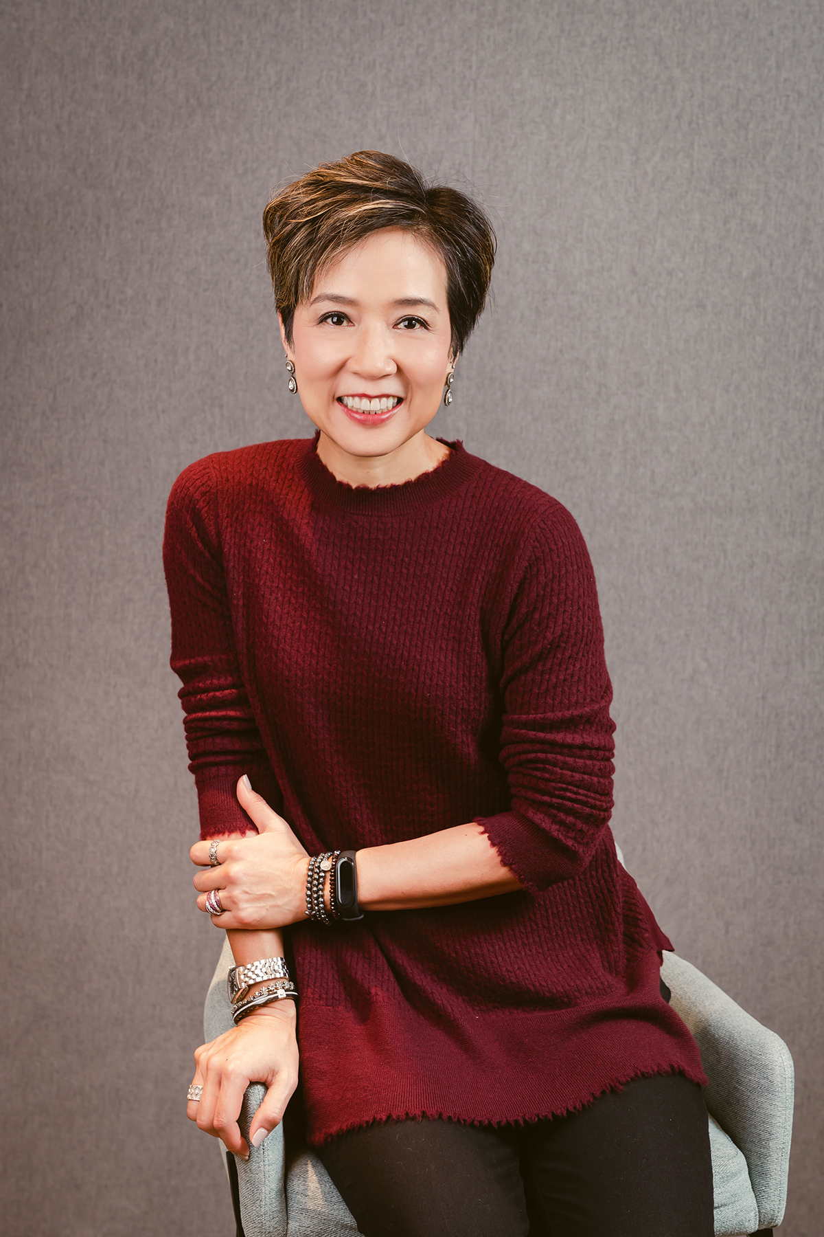 a woman in a red jumper sitting on a chair wearing bracelets and a watch