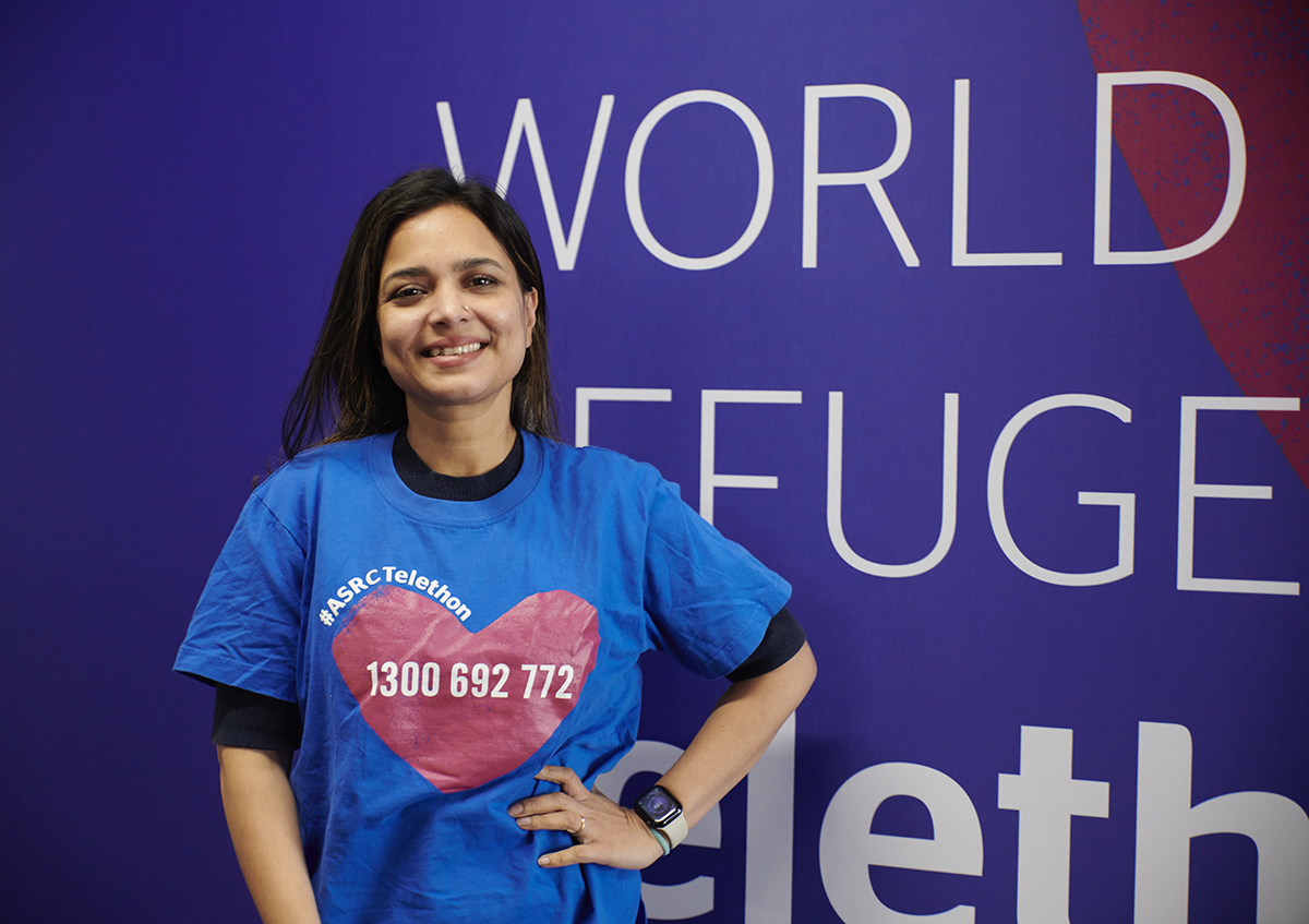 A woman standing in a blue t shirt next to a world refuge campaign board