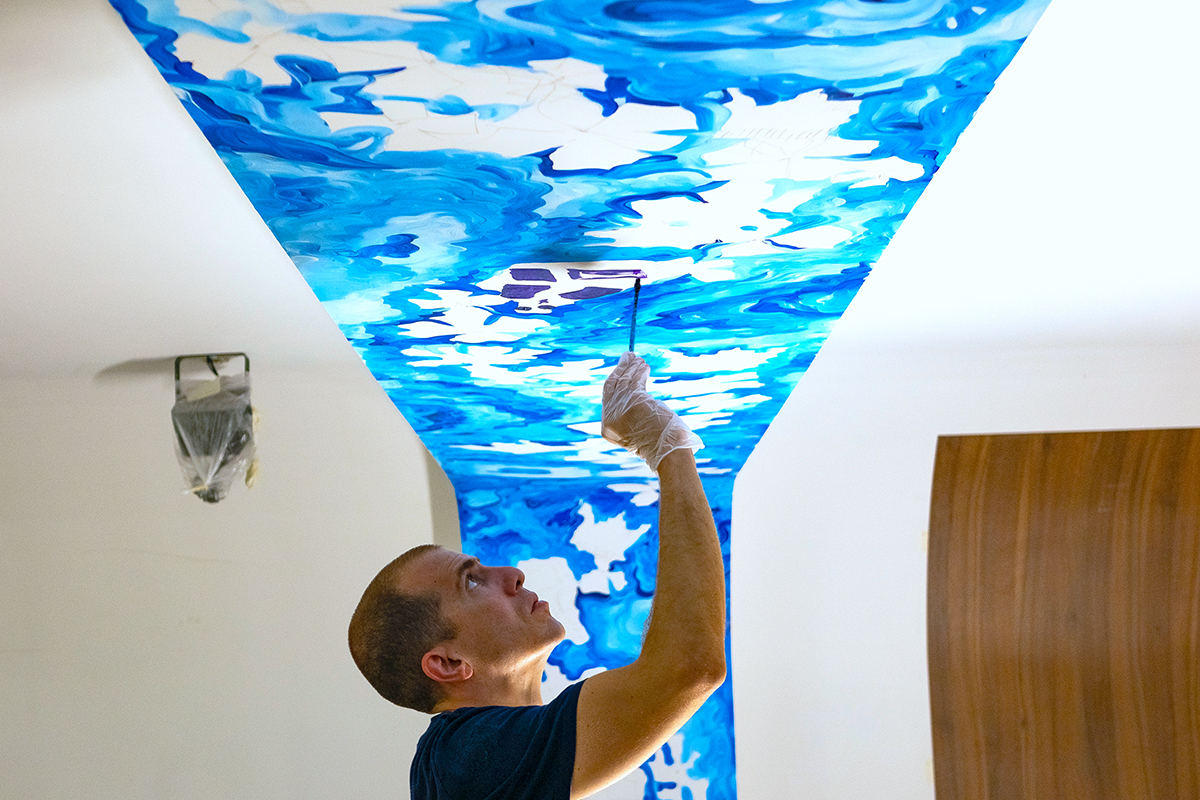 A man painting a blue mural on a ceiling