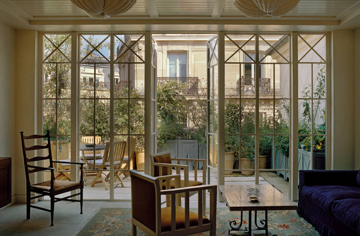 a room with wooden chairs and tables and a large glass window leading to a terrace
