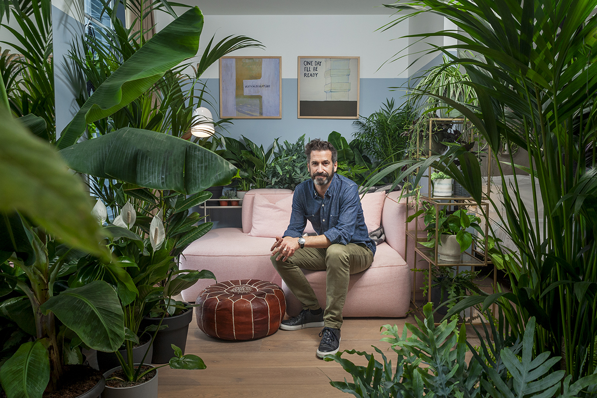 A man sitting on a pink couch with plants around him