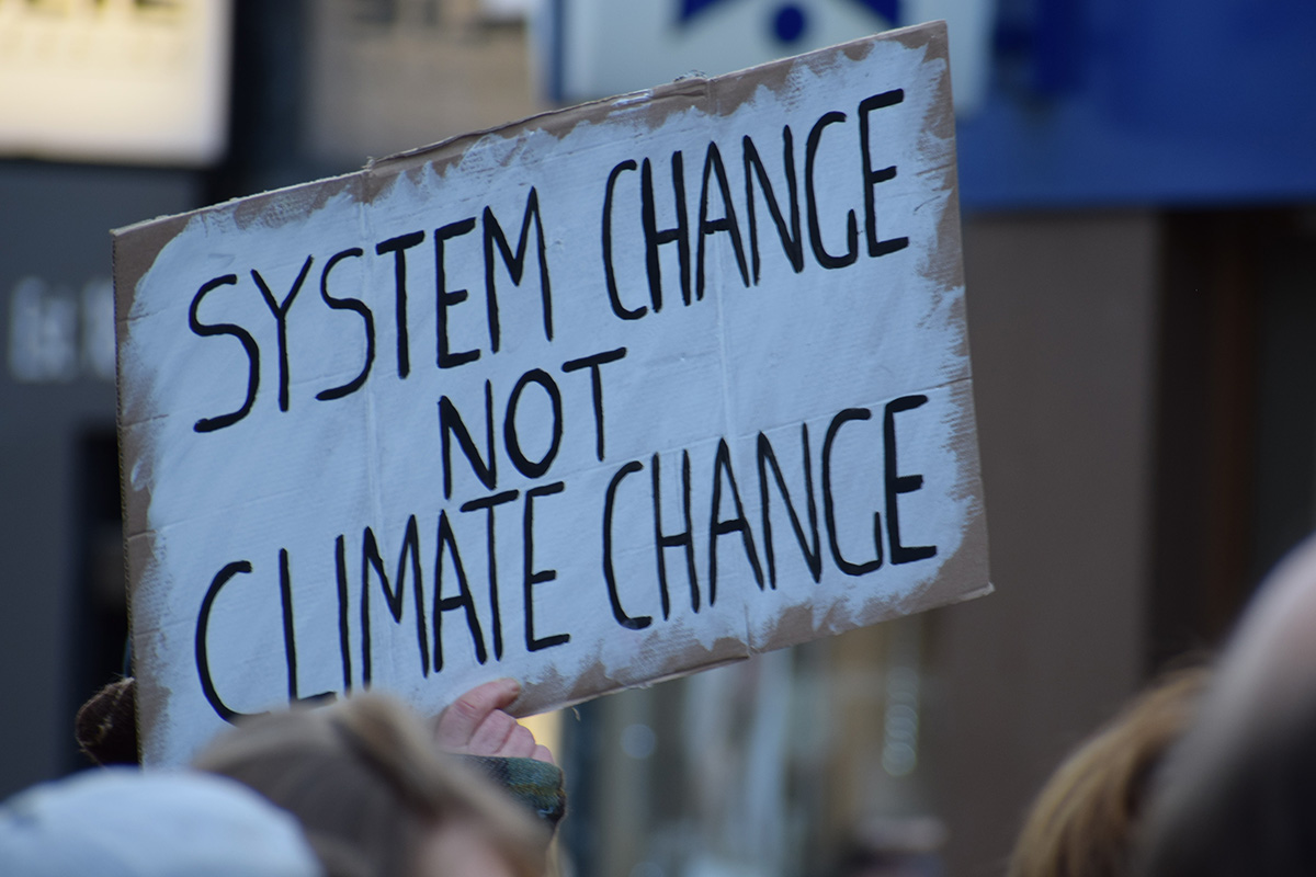 A white sign with black writing that says 'system change not climate change'