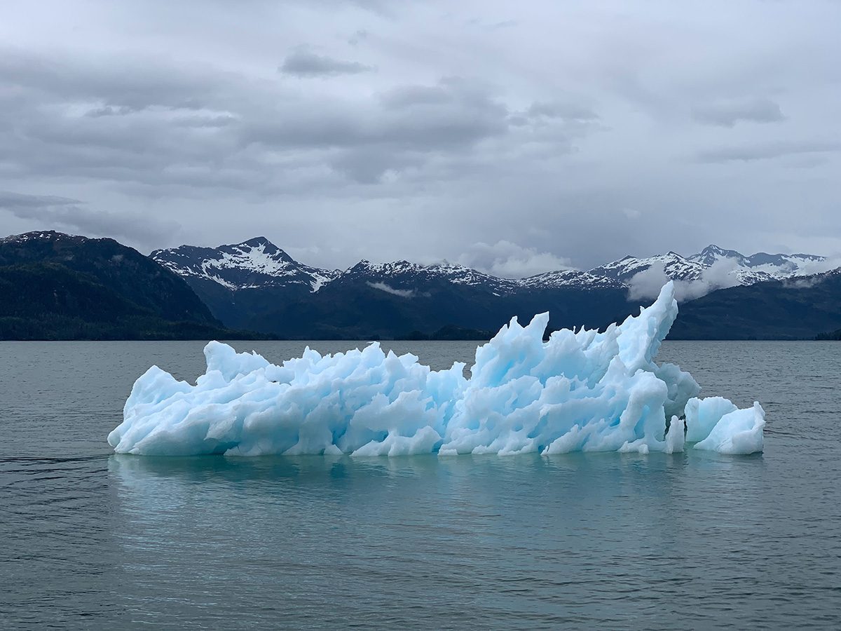 An iceberg melting in the sea with mountains in the background