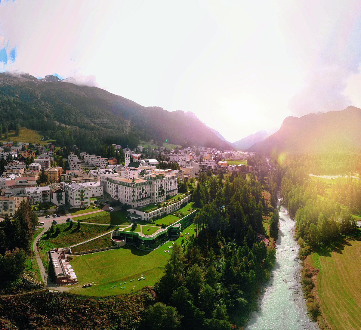 A palace surrounded by green grass, a river and mountains