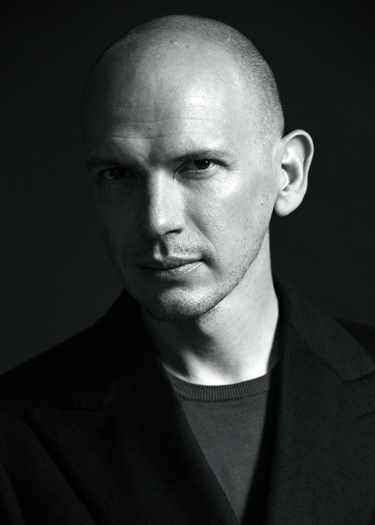 A bald man wearing a black t-shirt and blazer