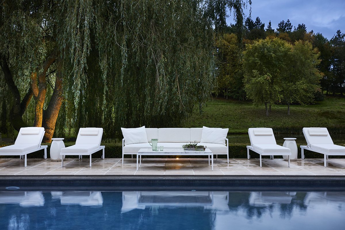 white lounge chairs by a swimming pool under a willow tree