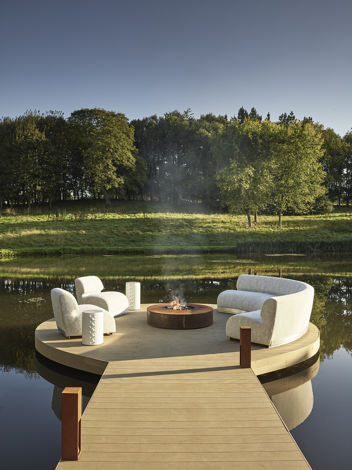 a deck on a lake with a fire and sofas in a circle at the end