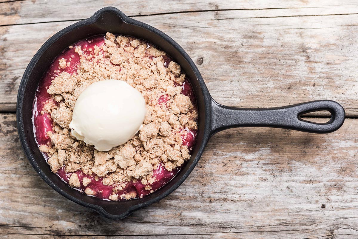 A berry crumble in a pan with a scoop of vanilla ice cream on top