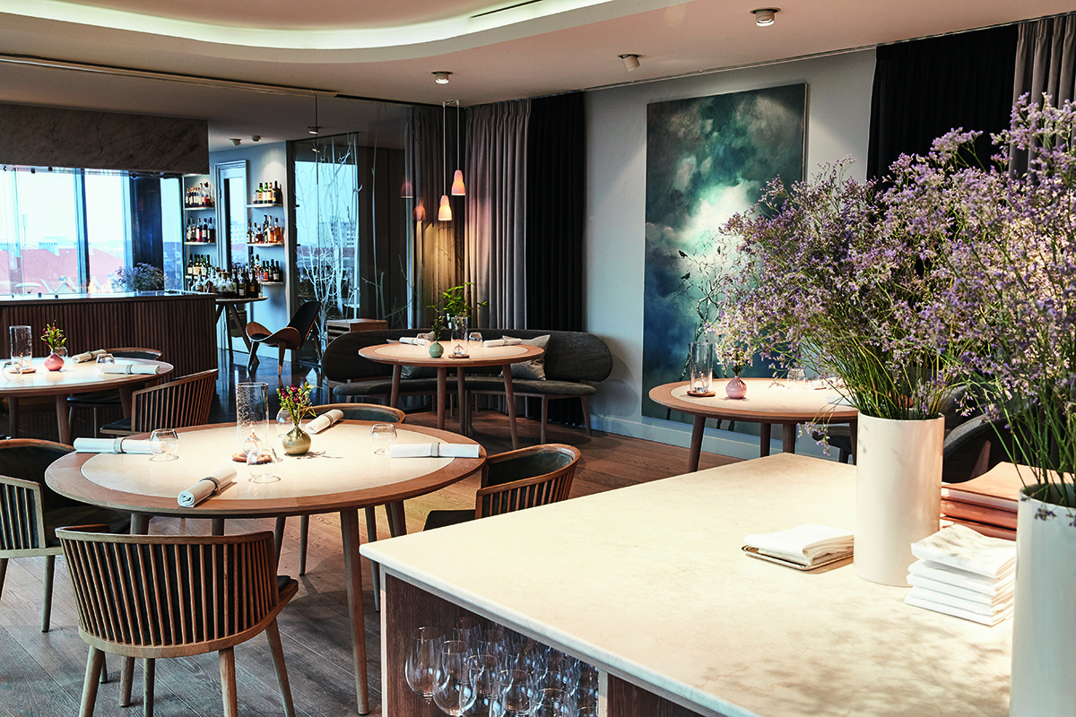 A restaurant with round wooden tables and grey chairs.