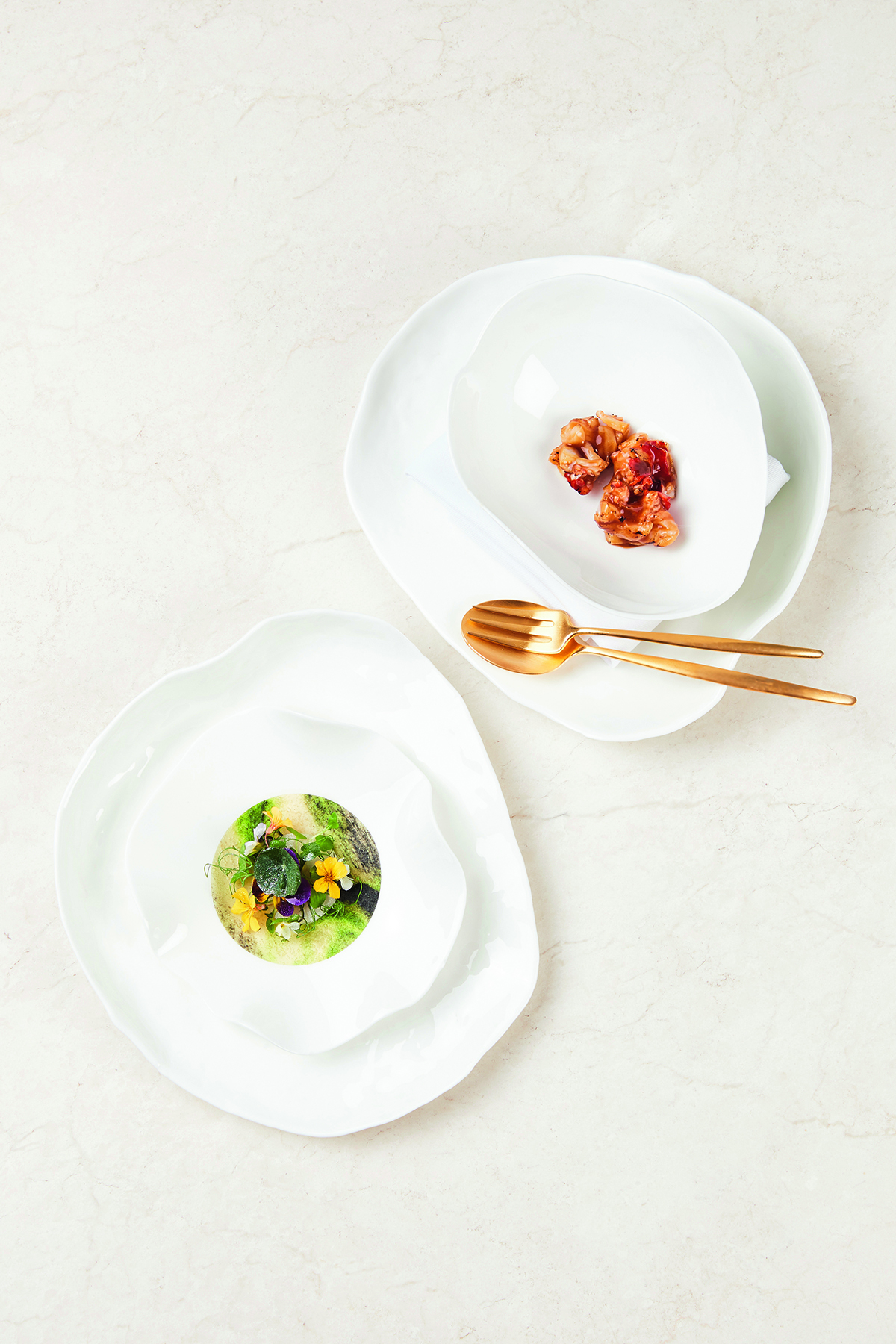 Two white plates and gold cutlery with onion and a green dish