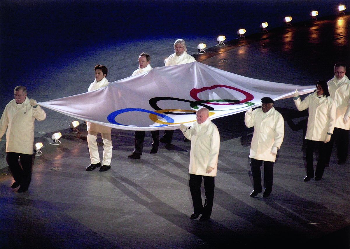 eight people carrying olympic flag 