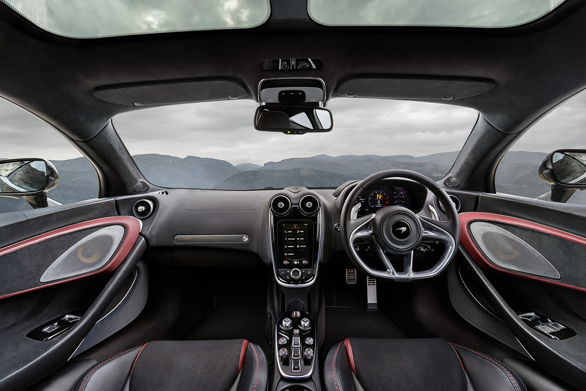 a red and black interior of a McLaren GT with mountains through the windscreen