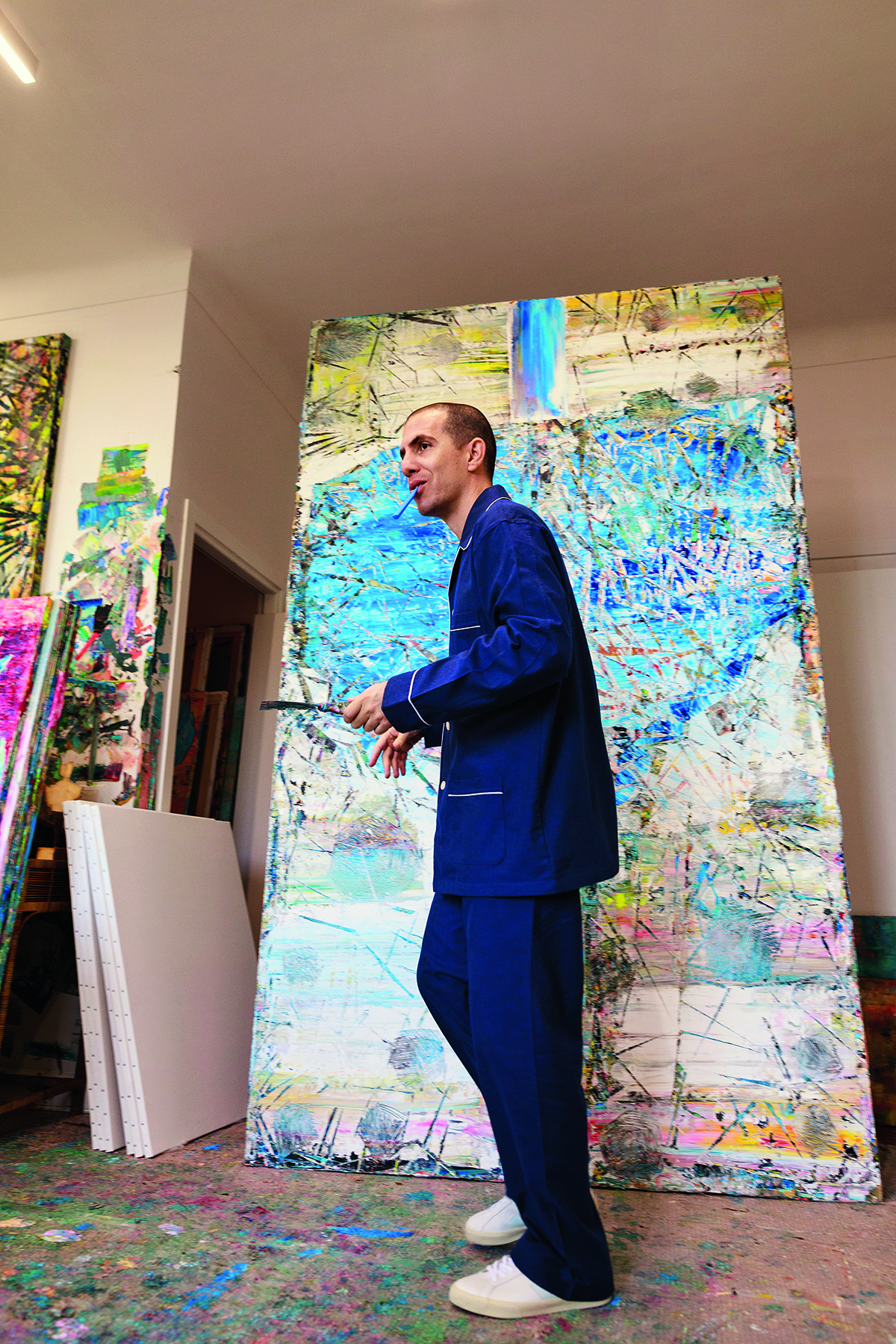 An artist in a studio standing in front of a multicoloured painted canvas