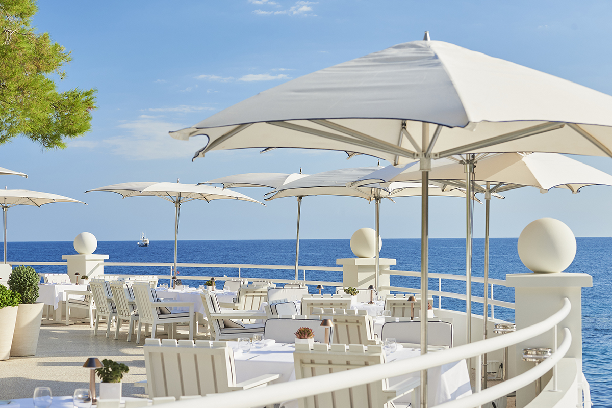 white umbrellas tables and chairs on a terrace overlooking the sea