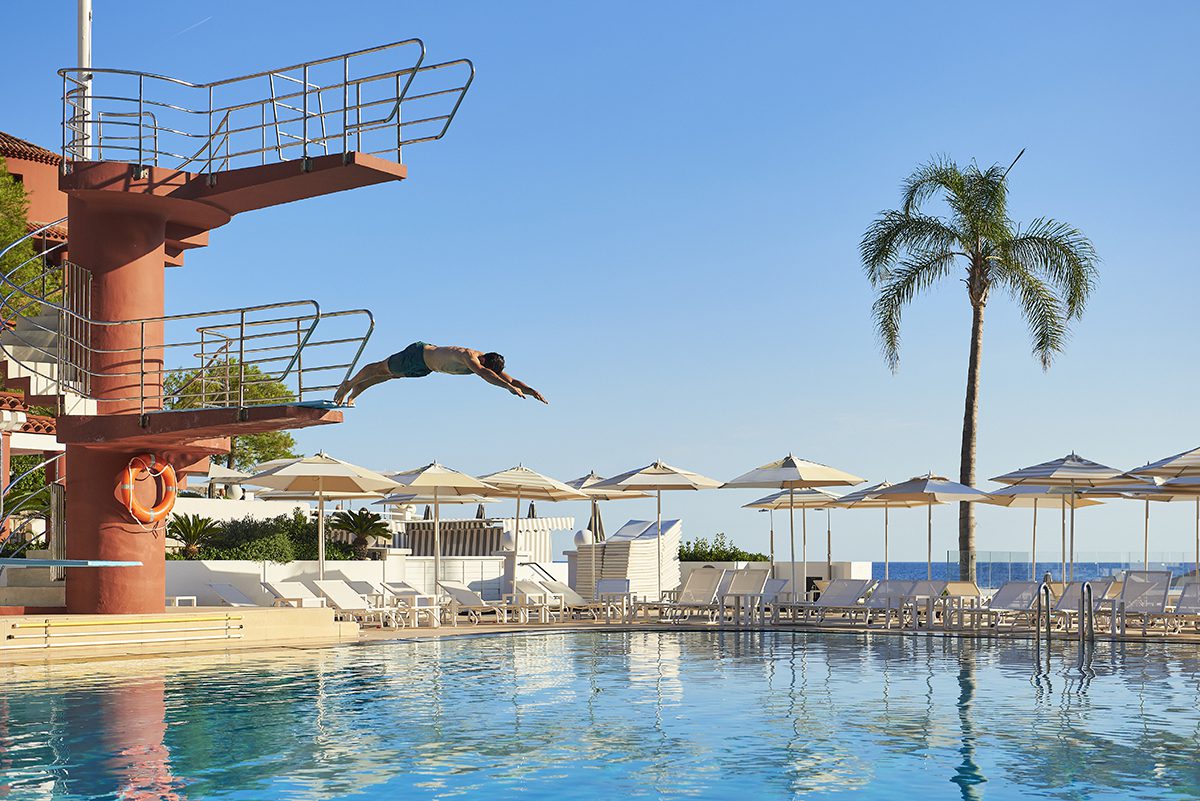 a pink diving board, a pool, parasols and deckchairs