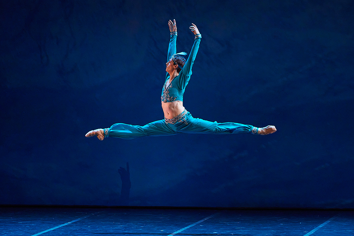 A man in a blue outfit doing a ballet jump in the air