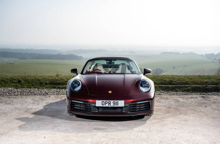 a red convertible Porsche parked in front of a green field