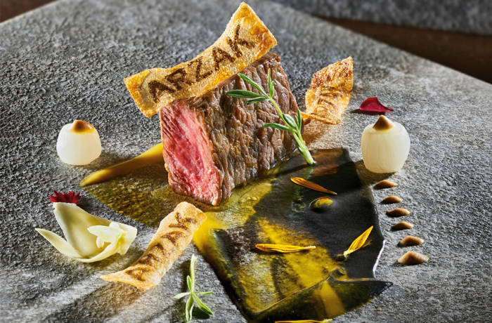 A steak on a plate with a cracker that has the words ARZAK burnt into it