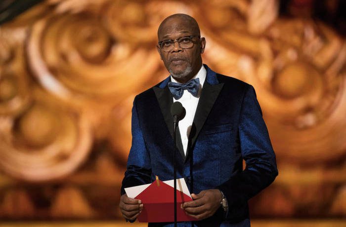 A man wearing a navy blue suit presenting an award