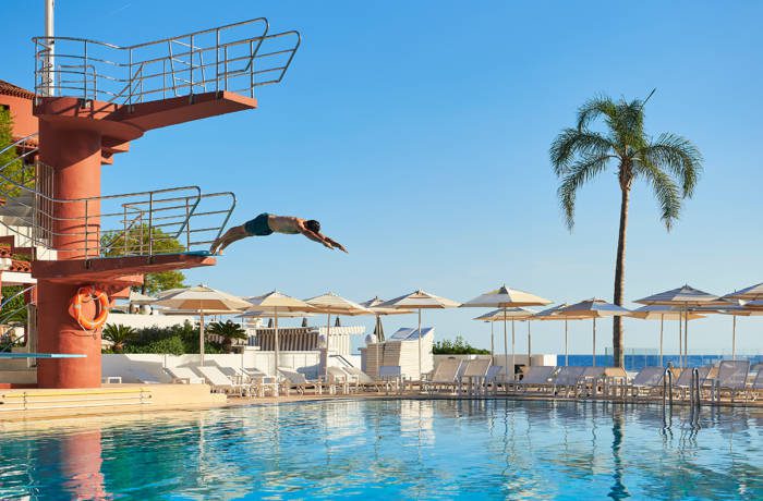 a pink diving board, a pool, parasols and deckchairs