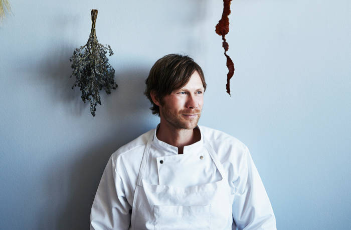 A chef in an apron standing by a wall with geranium hanging by him