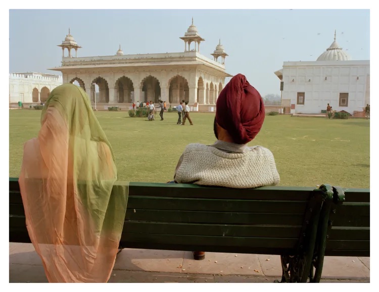 A man and woman sitting on a bench looking at a palace