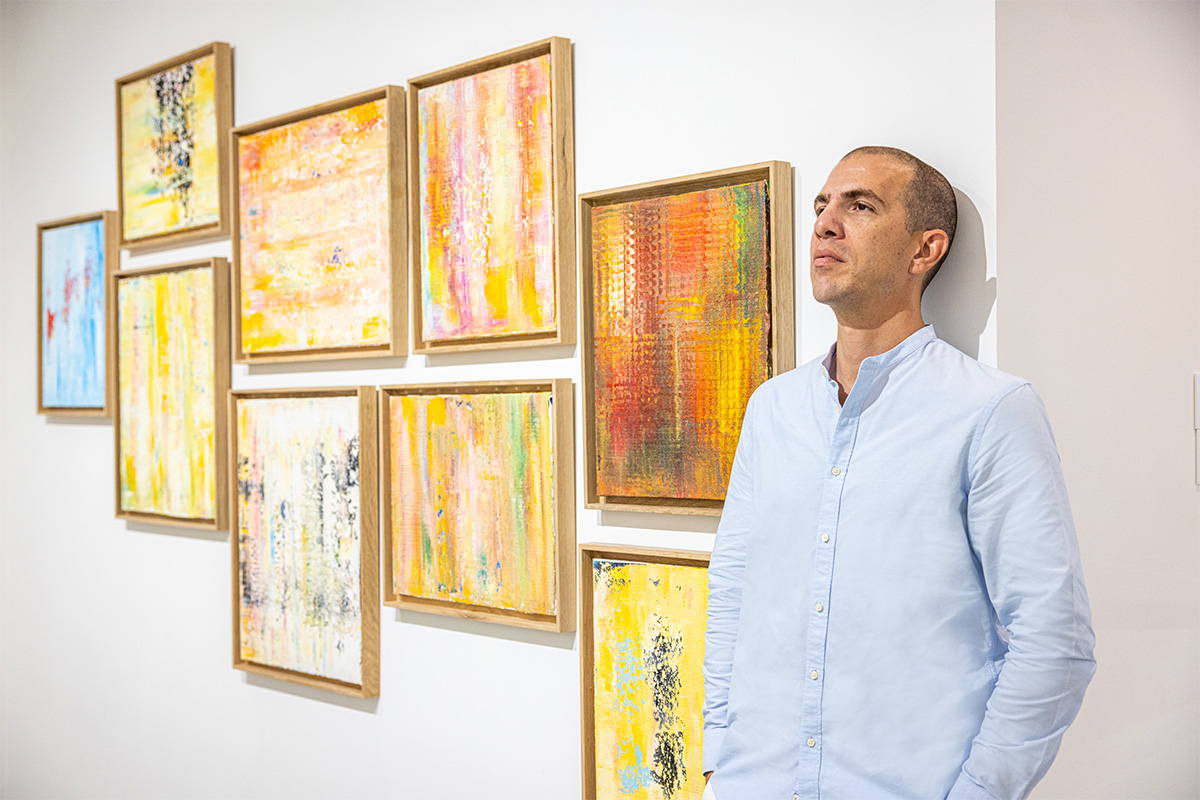 a man in a blue shirt standing next to yellow paintings