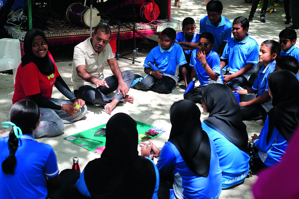 A group of school children in blue uniforms sitting in a circle having a lesson
