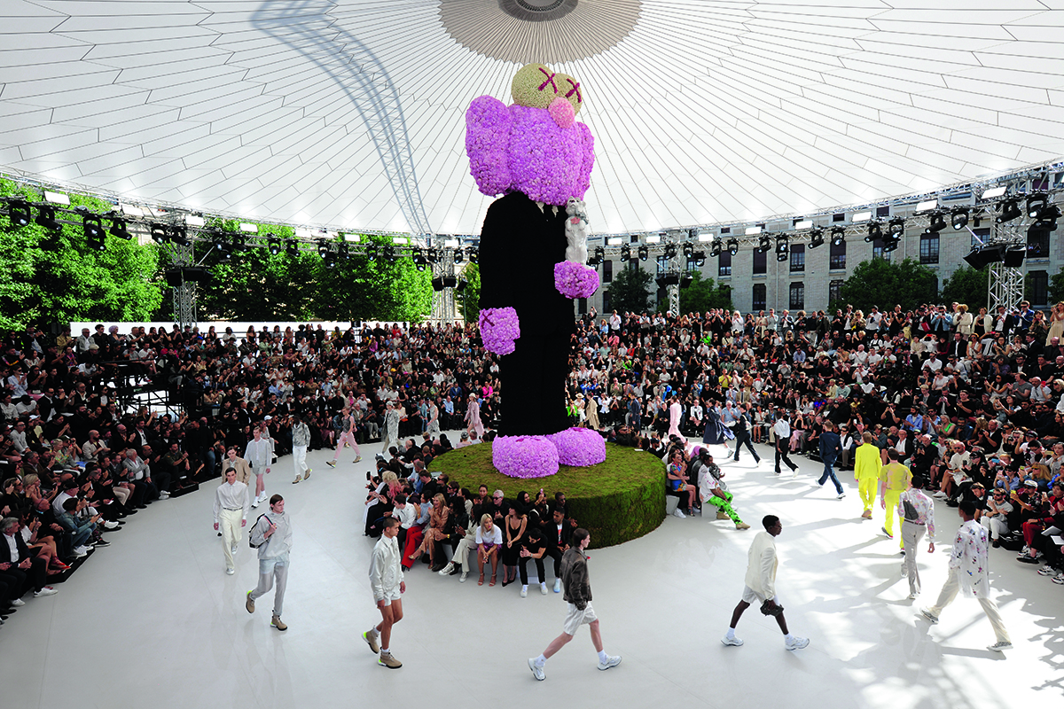 A sculpture of a pink standing elephant in a black suit with models walking around it