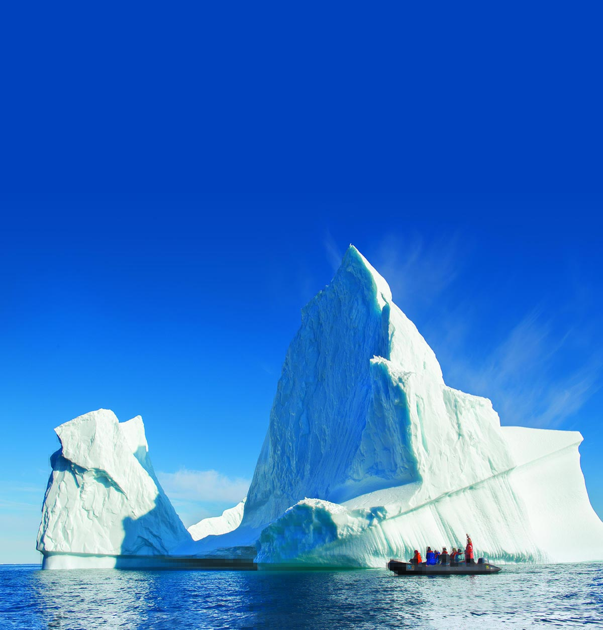 An iceberg in the sea with people looking at it from a speed boat