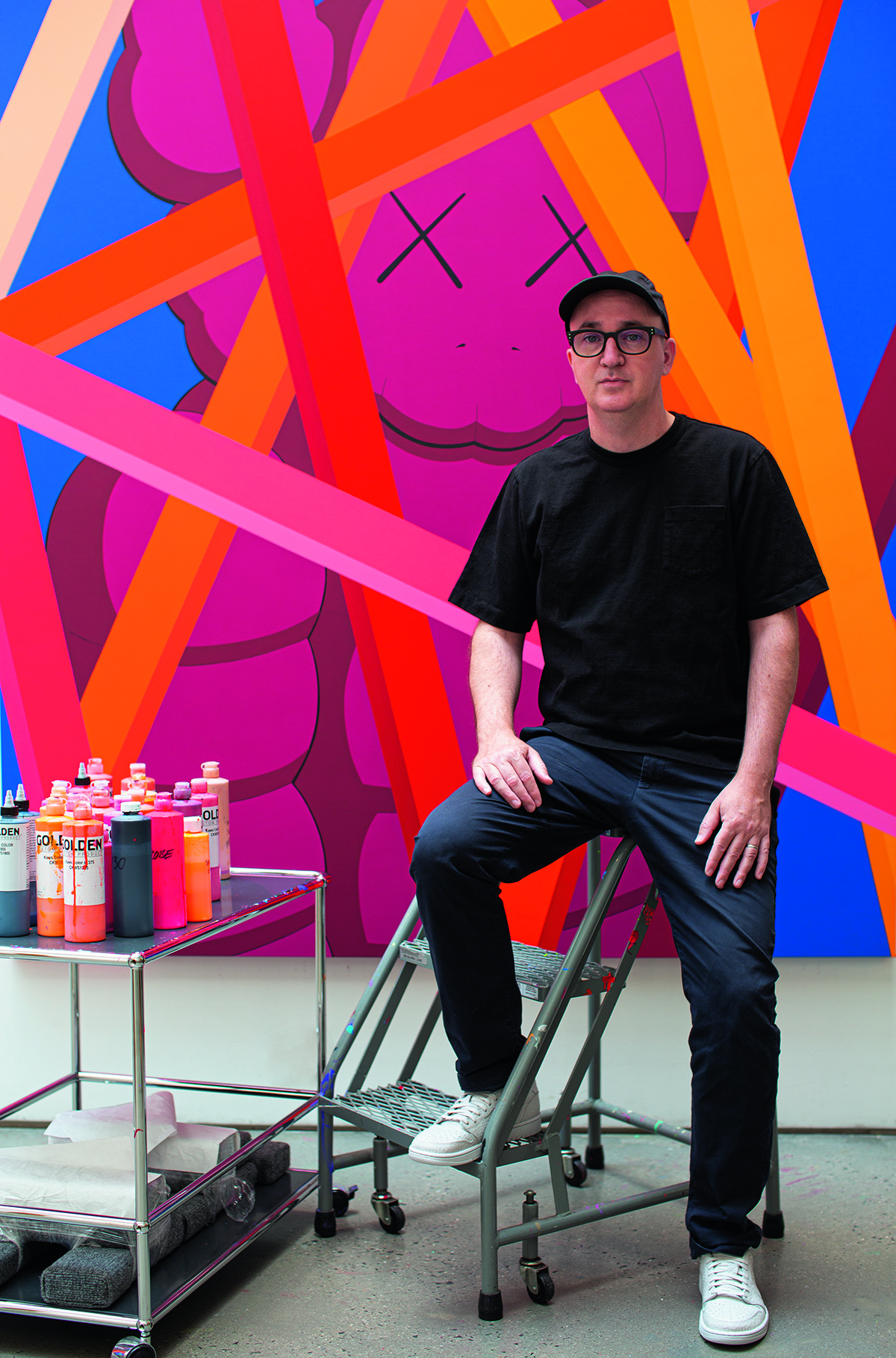 A man sitting on a stool next to his paints and a colourful wall