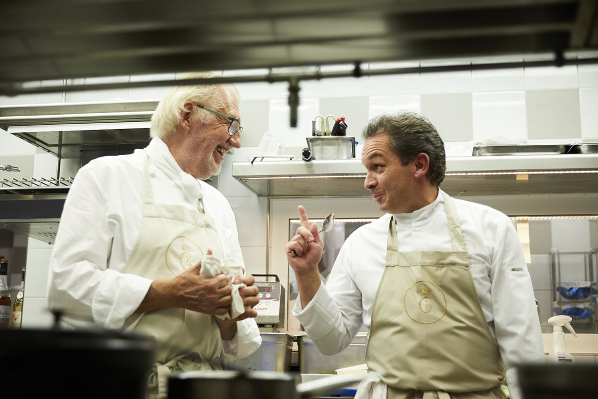 two chefs working in a kitchen with beige aprons 