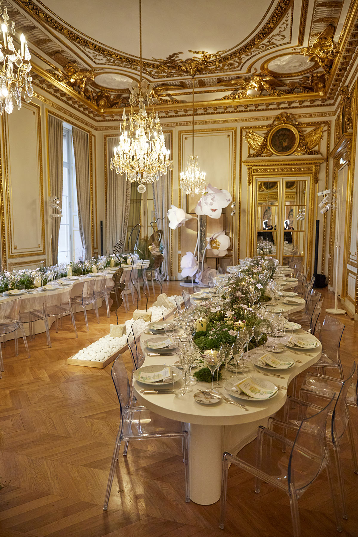 A dinner table in a white and gold room with flowers along the tables