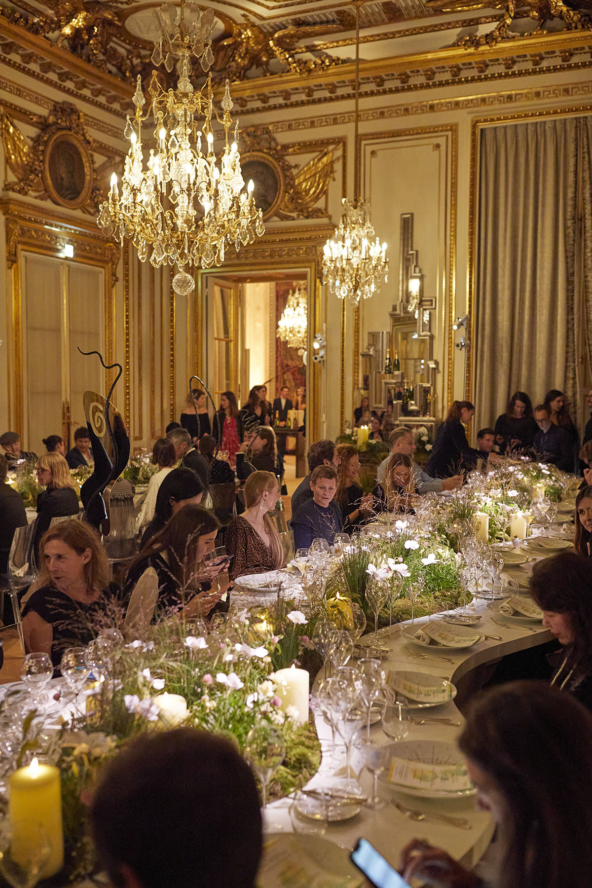 people sitting around a table, having dinner with flowers in the middle