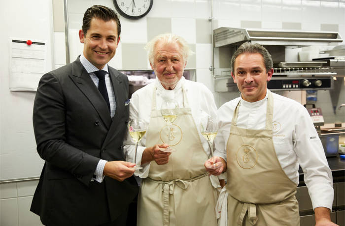 two chefs and a man in a suit holding glasses of champagne smiling at the camera