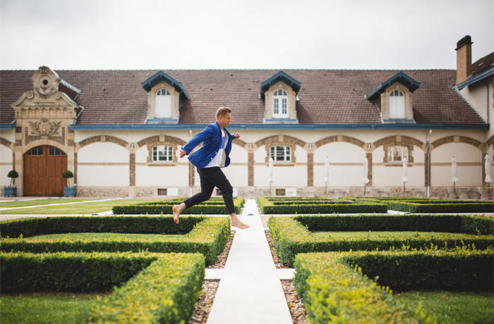 A man in a blue jacket jumping over small hedges in front of a house
