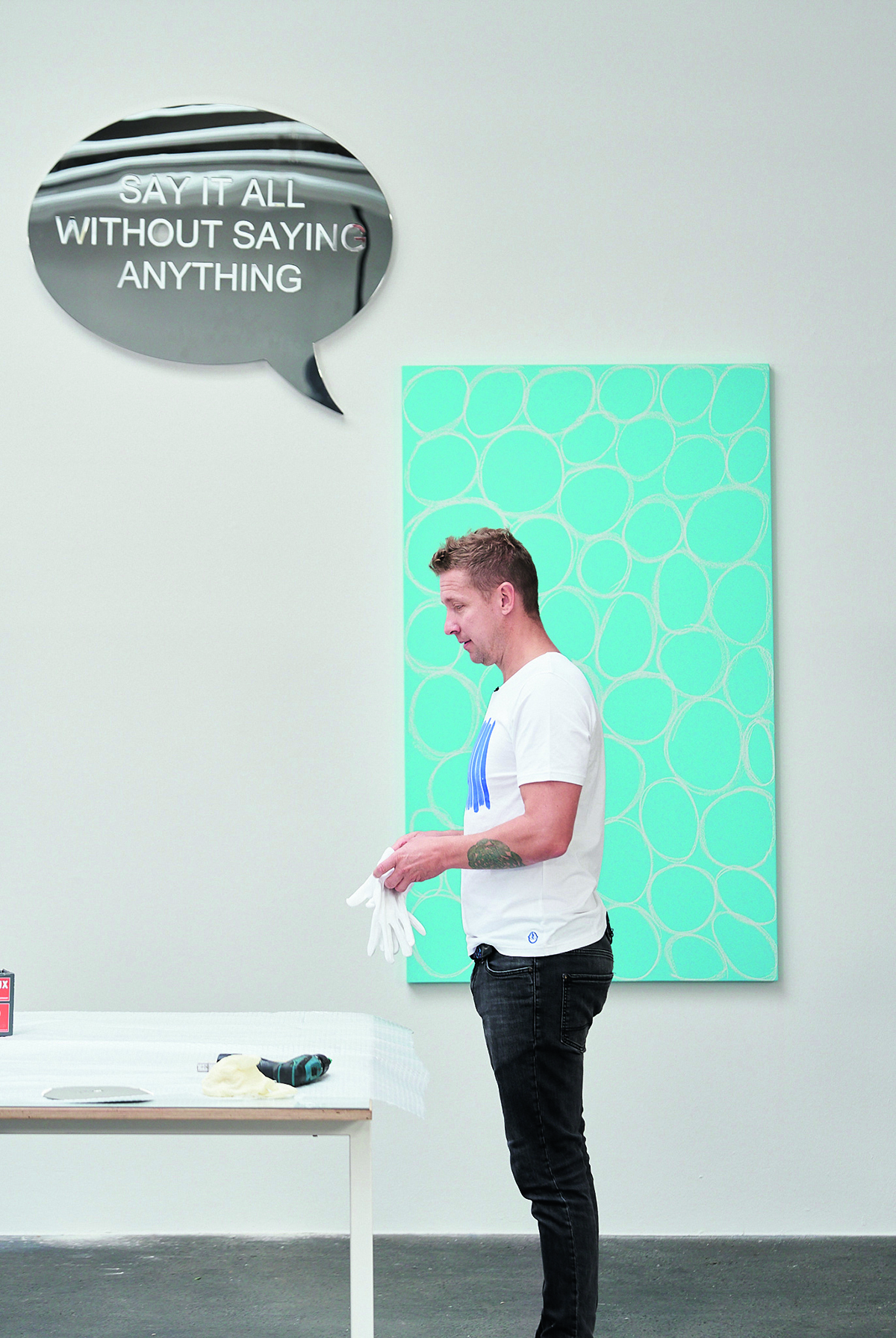  A man standing next to a bleu canvas and a speech bubble on top of his with words in it