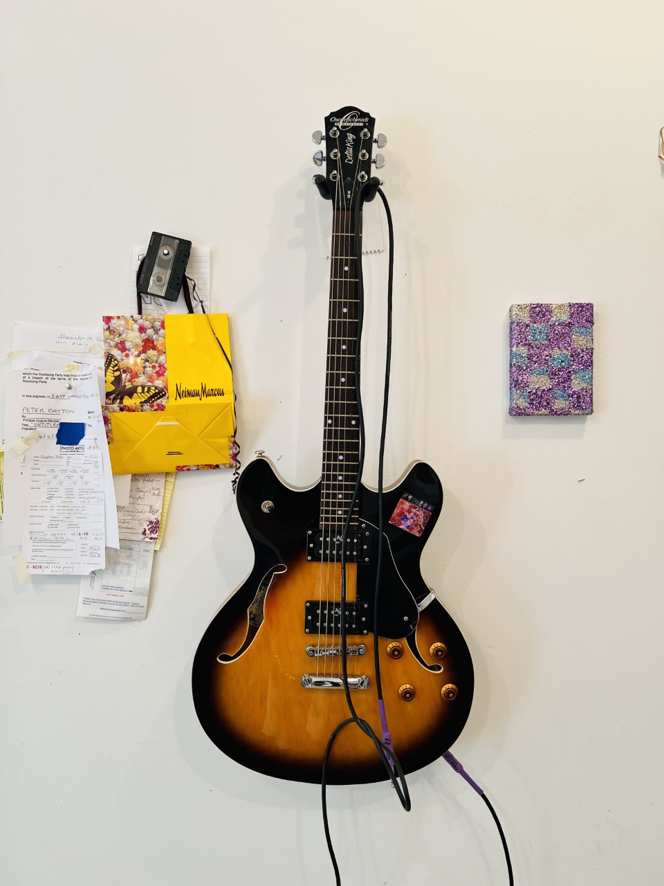 A guitar hanging on the wall by a small piece of art