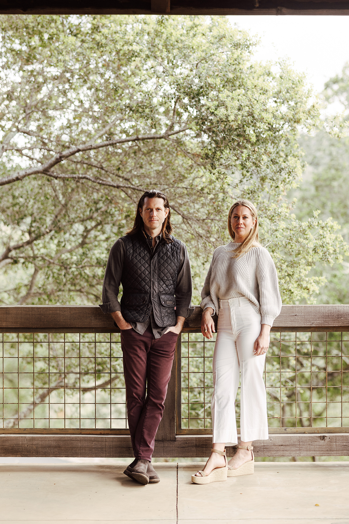 A man in red trousers and a grey shirt standing next to a woman in a white shirt and trousers standing on a terrace