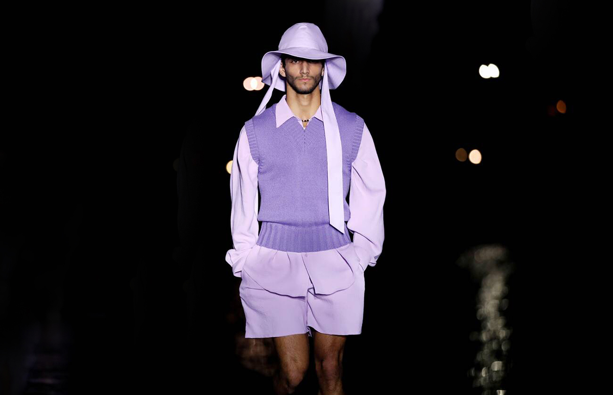 A man wearing purple shorts, hat, vest and shirt on a dark runway