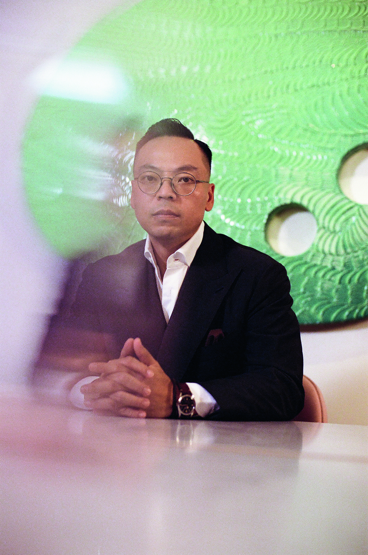 A man wearing a suit sitting in front of a green piece of art