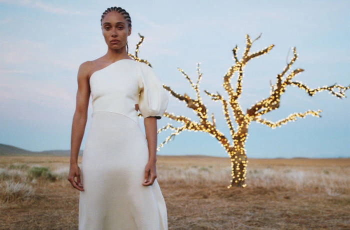A woman wearing a white dress standing next to a lit up tree in a desert