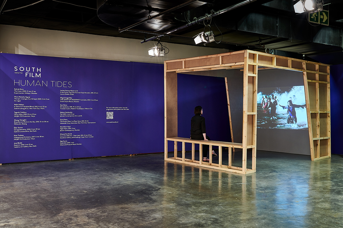A projected screen under a wooden canopy in front of a purple wall in a gallery