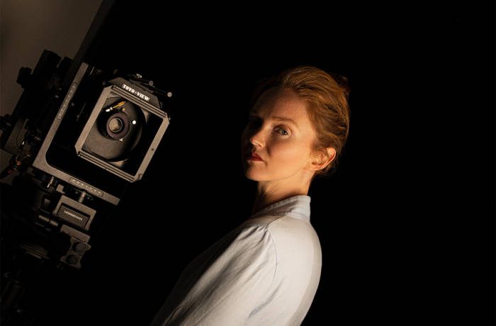 A ginger model with a wearing a white shirt with a camera next to her head