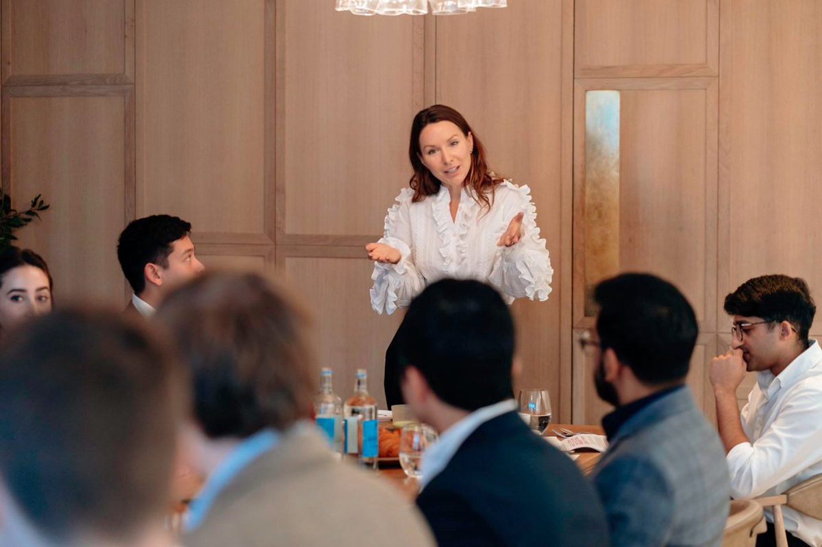 A woman wearing a white shirt giving a talk in a boardroom to a group of men