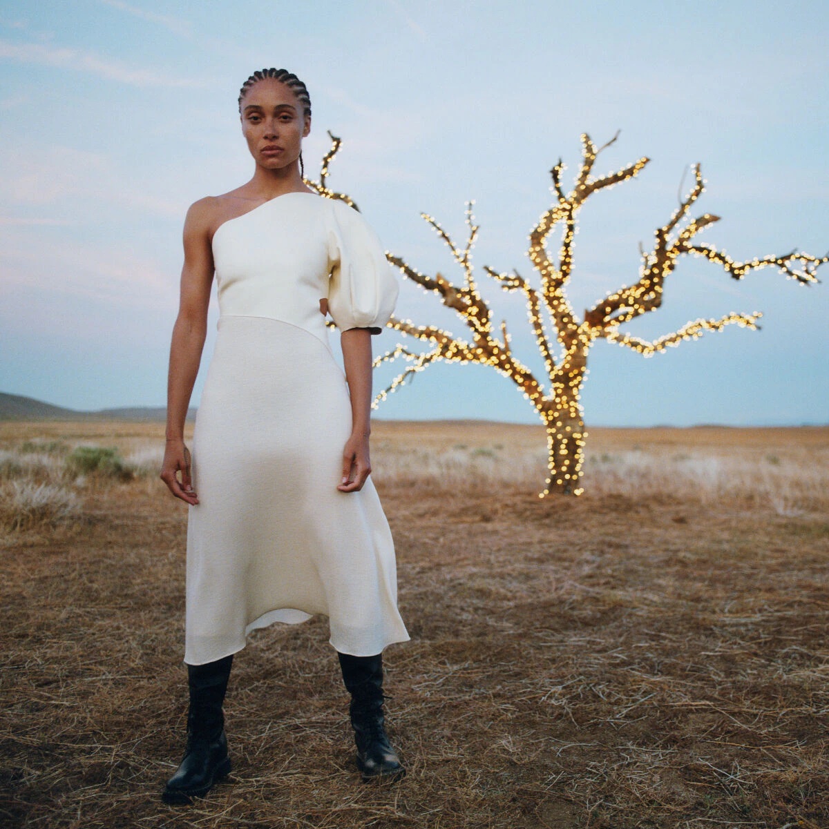 A woman wearing a white dress standing next to a lit up tree in a desert