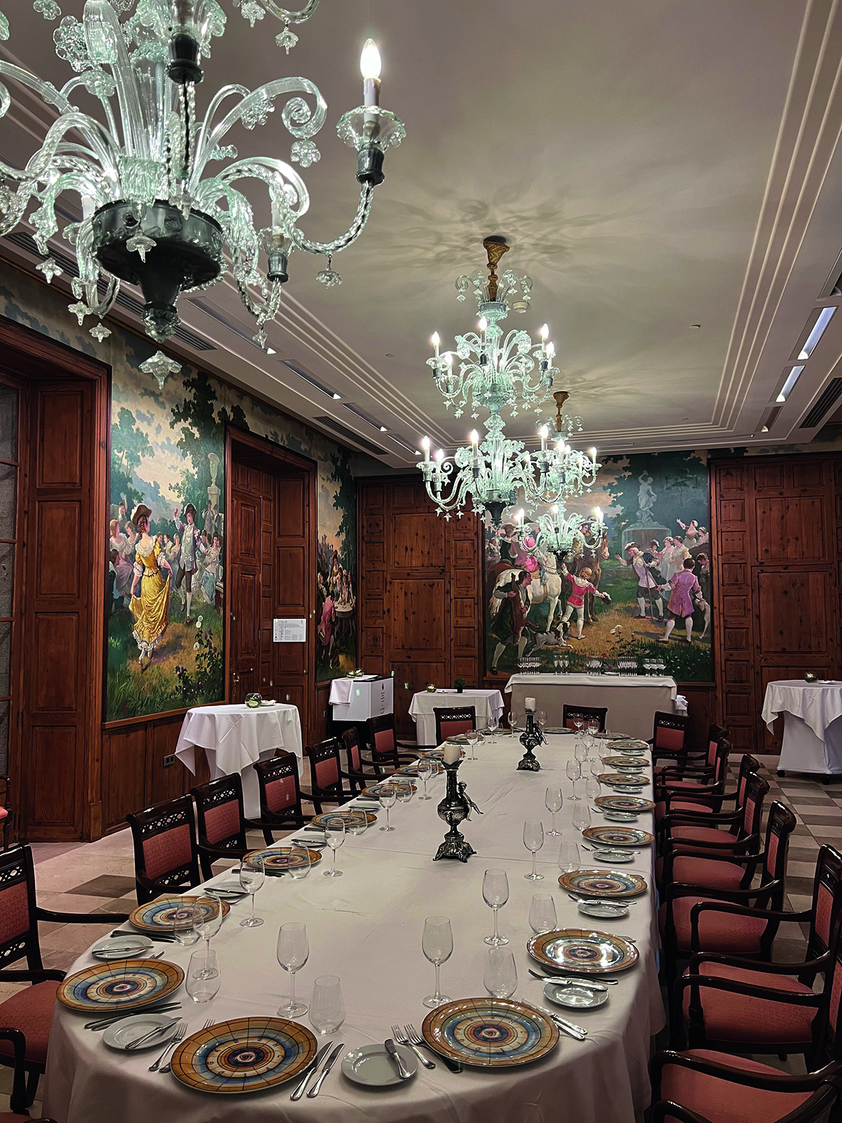 A dining room with wooden walls and large glass chandeliers over the table