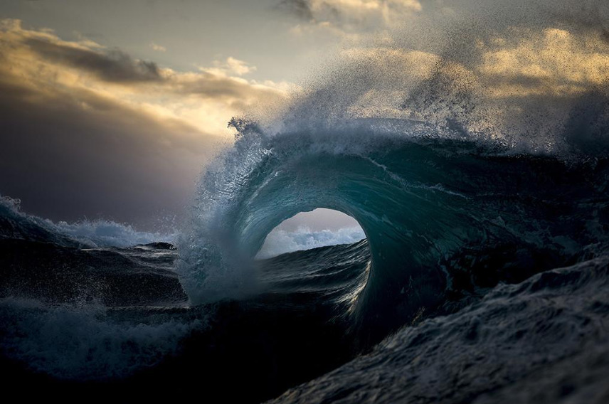 A wave crashing into the sea with clouds above it