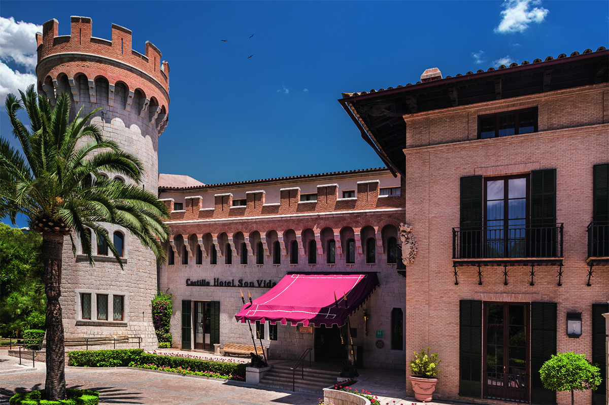 A hotel building with a red awning at the entrance and turrets around the roof and a palm tree